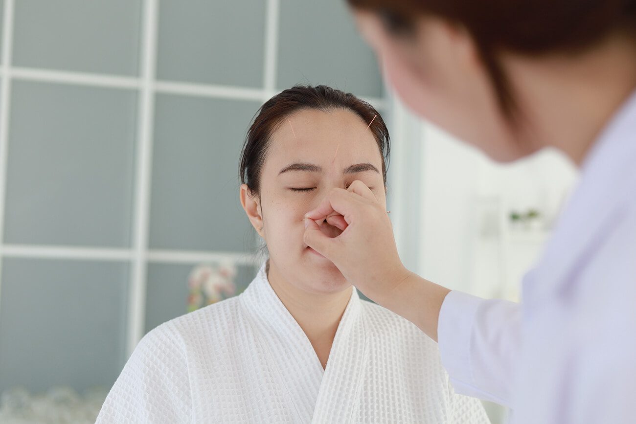 hand doctor performing acupuncture therapy asian female undergoing acupuncture treatment with line fine needles inserted into her face skin clinic hospital