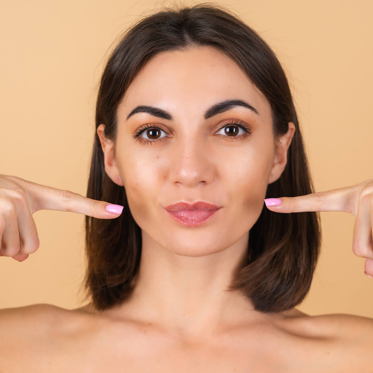 portrait young woman beige with natural makeup with bare shoulders points her fingers lips